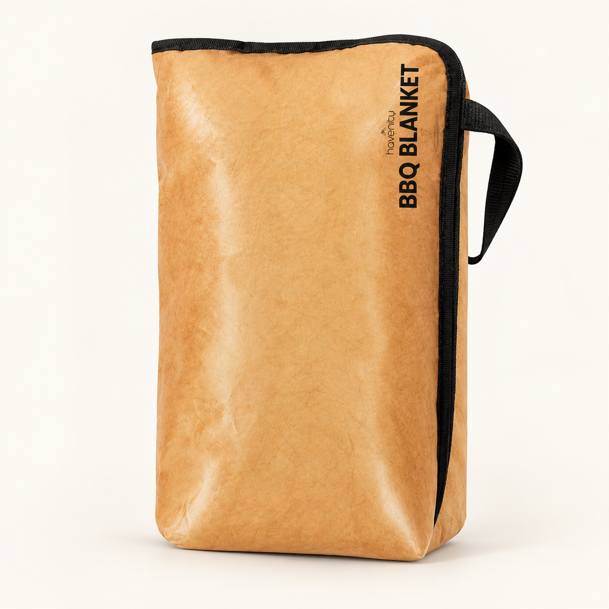 The kraft-tan BBQ Blanket resting bag standing upright on a warm off-white studio background, with its black zipper edge and loop handle visible.