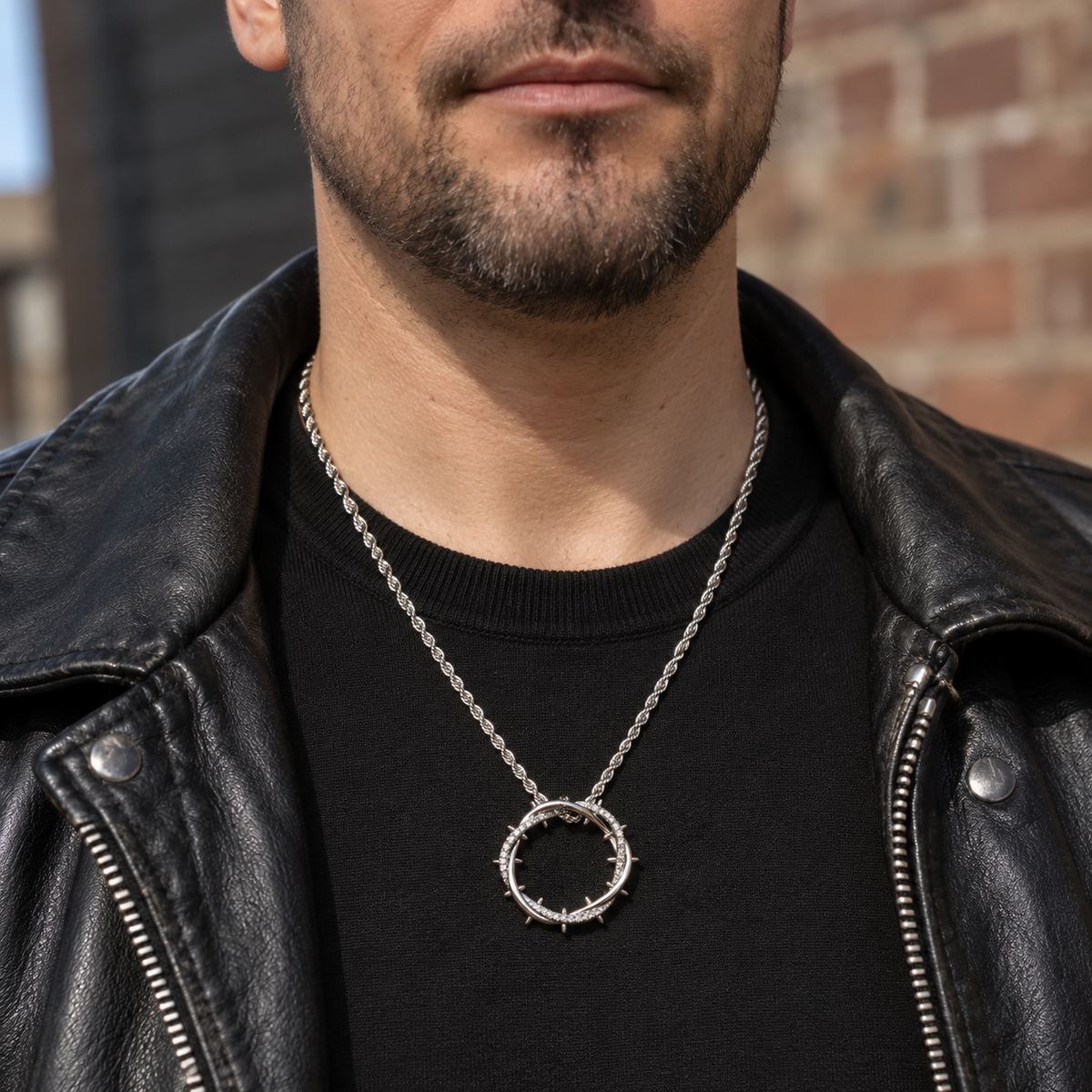 Man in a black knit and leather jacket wearing the silver crown of thorns pendant at mid-chest.
