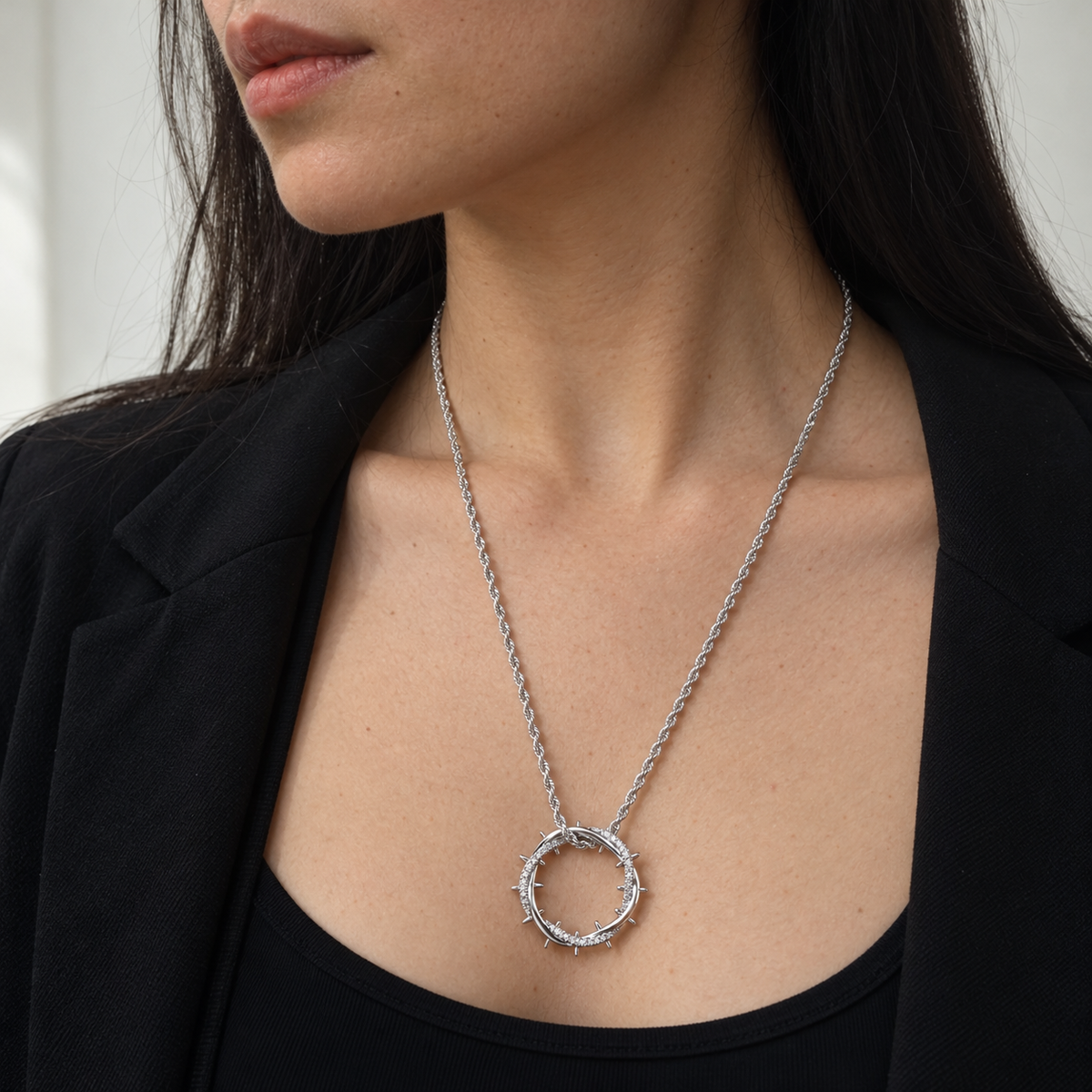 Woman in a black blazer wearing the silver crown of thorns pendant just below her collarbone.