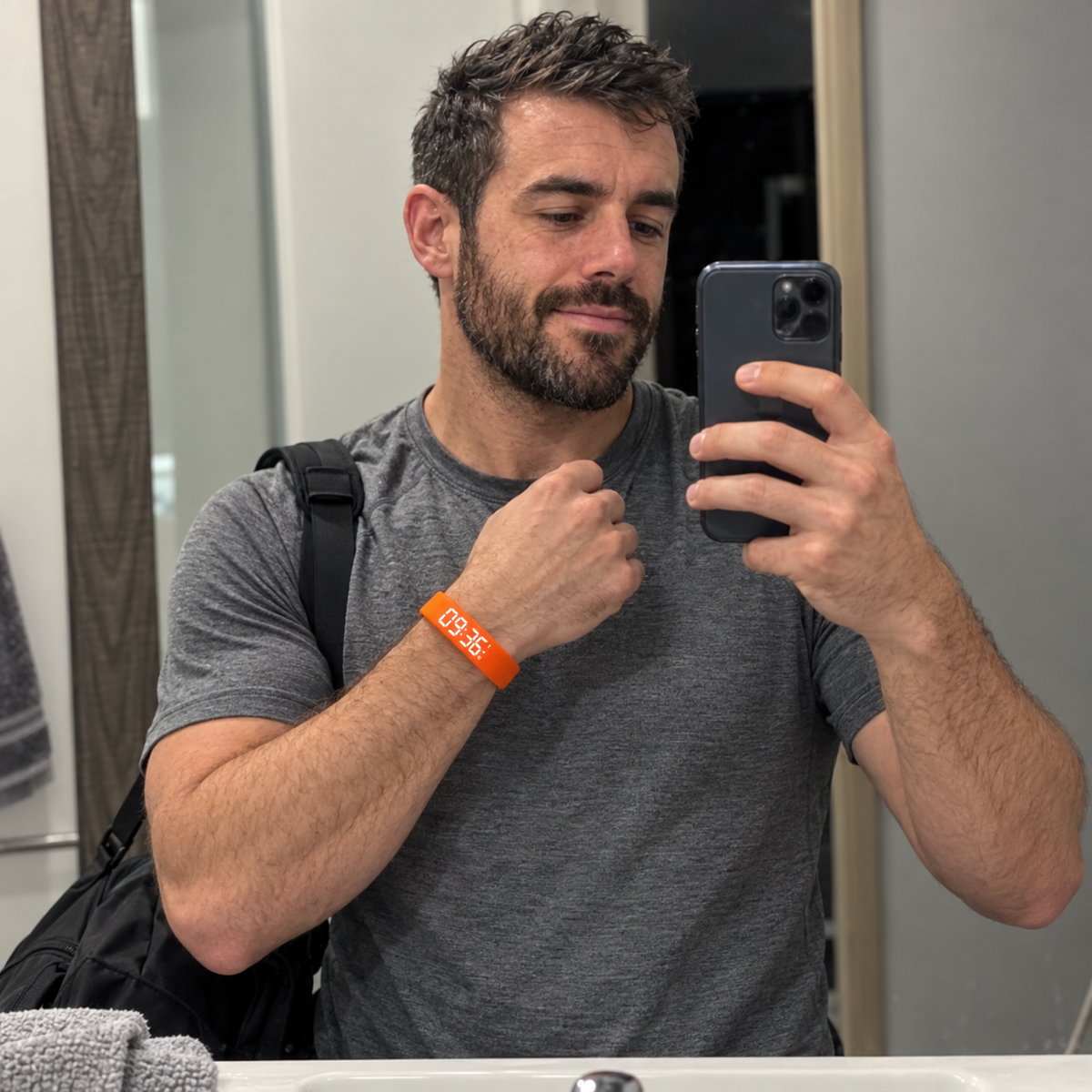 A man in gym clothes takes a mirror selfie early in the morning, showing an orange activity band on his wrist.
