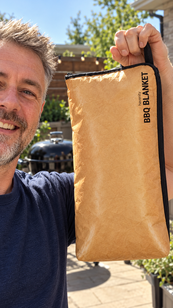 A smiling man in his fifties holds up the zipped BBQ Blanket by its handle in his sunny backyard.