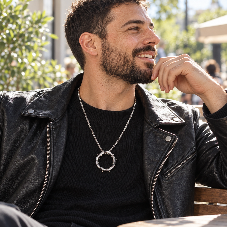 A bearded man in a black leather jacket wears the silver Crown of Thorns Necklace at an outdoor café.