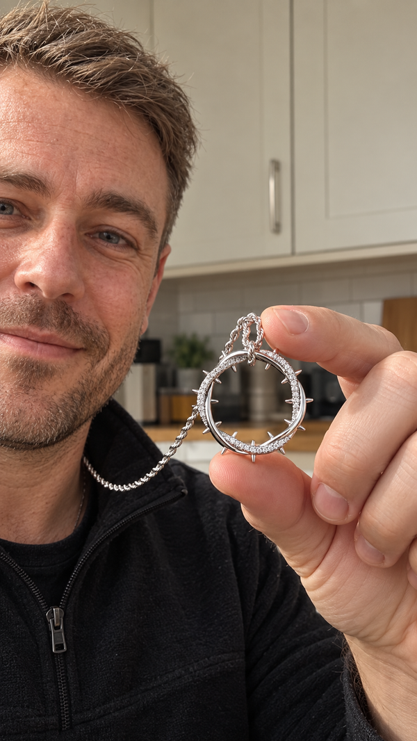 A man takes a selfie at home holding up the silver Crown of Thorns pendant between his fingers.