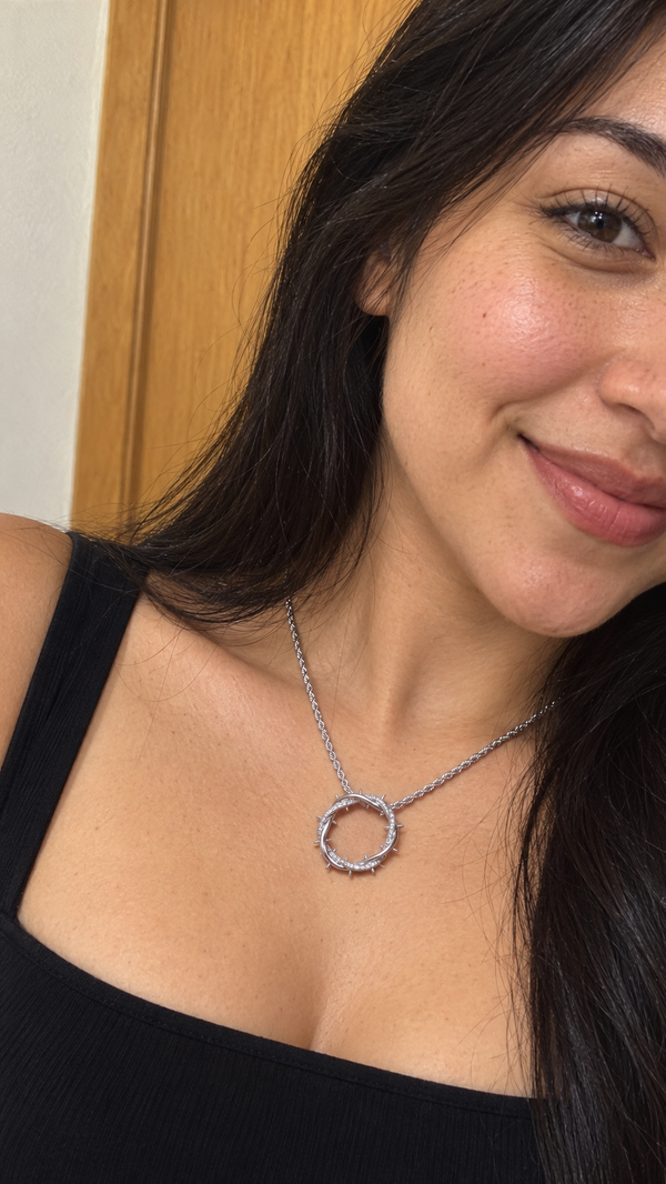A smiling woman in a black top wears the silver Crown of Thorns pendant just below her collarbone.