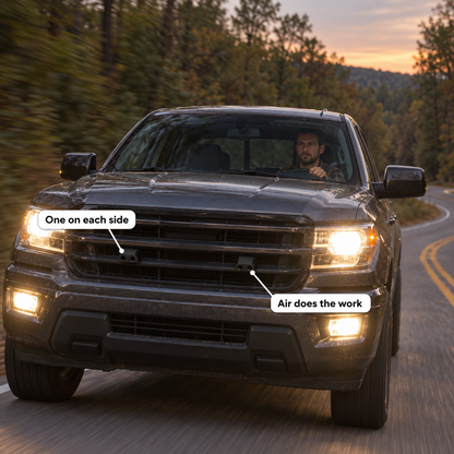 A pickup truck on a wooded country road at dusk with a deer whistle on each side of the grill.