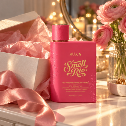 The pink Strawberry Gummies perfume bottle on a vanity beside an open gift box with pink tissue paper and flowers.