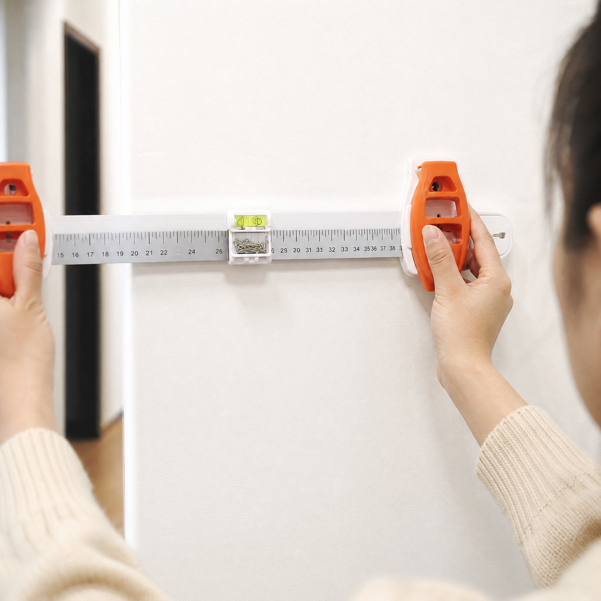 Hands pressing the orange tool handle to set a nail in a white wall.