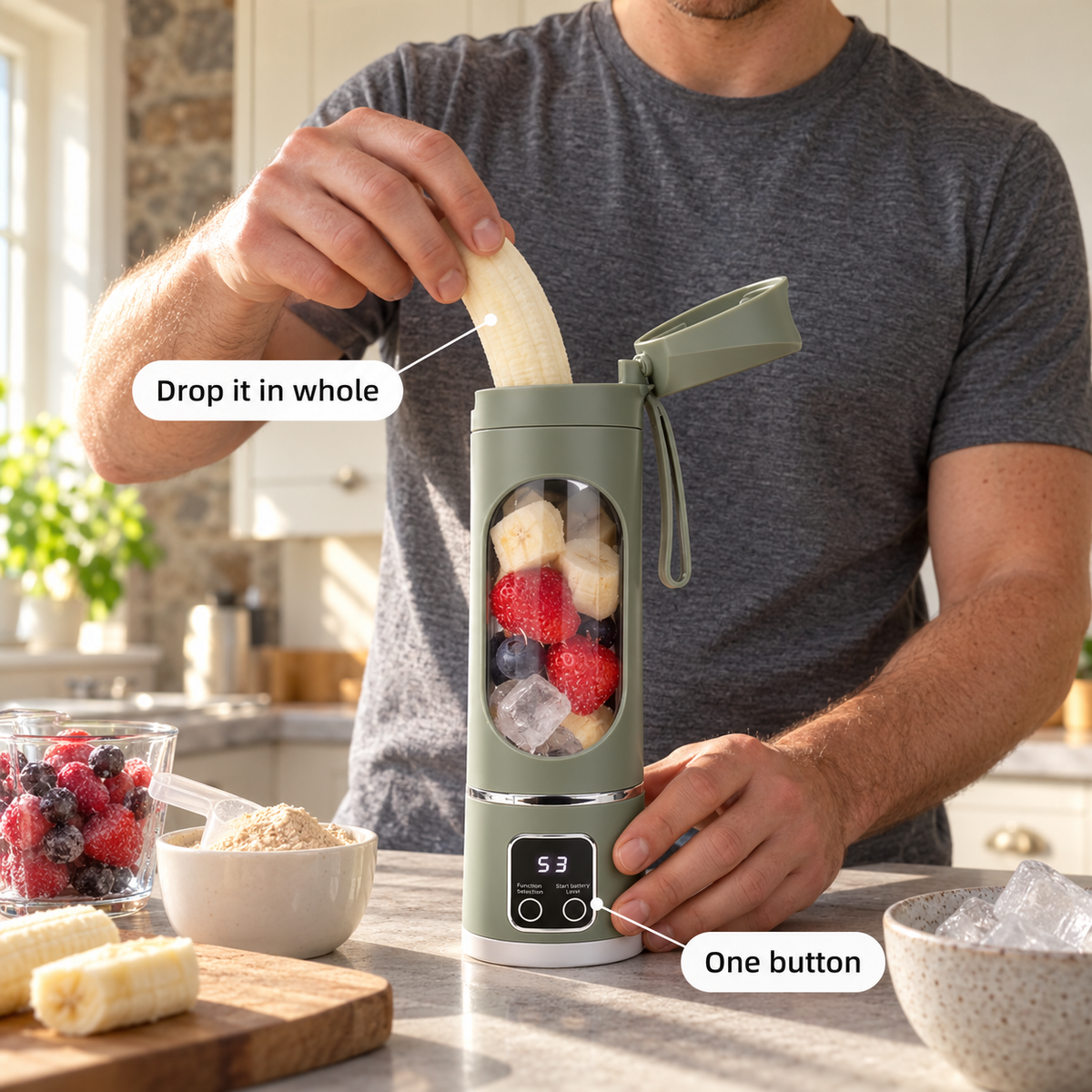 A man drops a whole banana into a sage green portable blender on a kitchen counter next to protein powder and frozen berries.